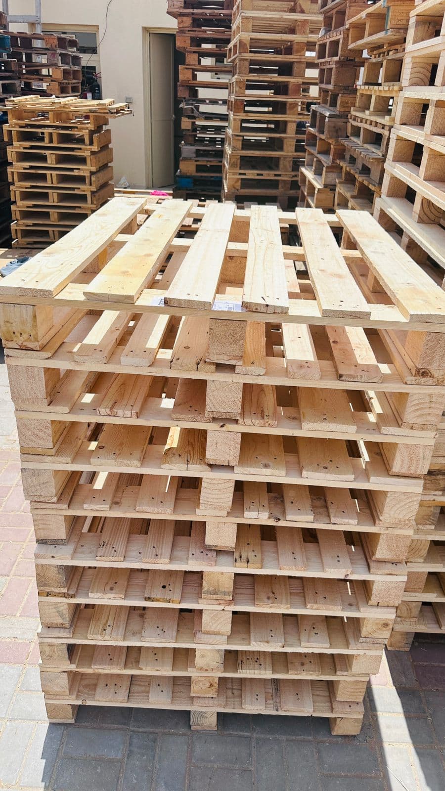 A tall stack of heavy-duty wooden pallets with close-spaced deck boards in the Sharjah yard