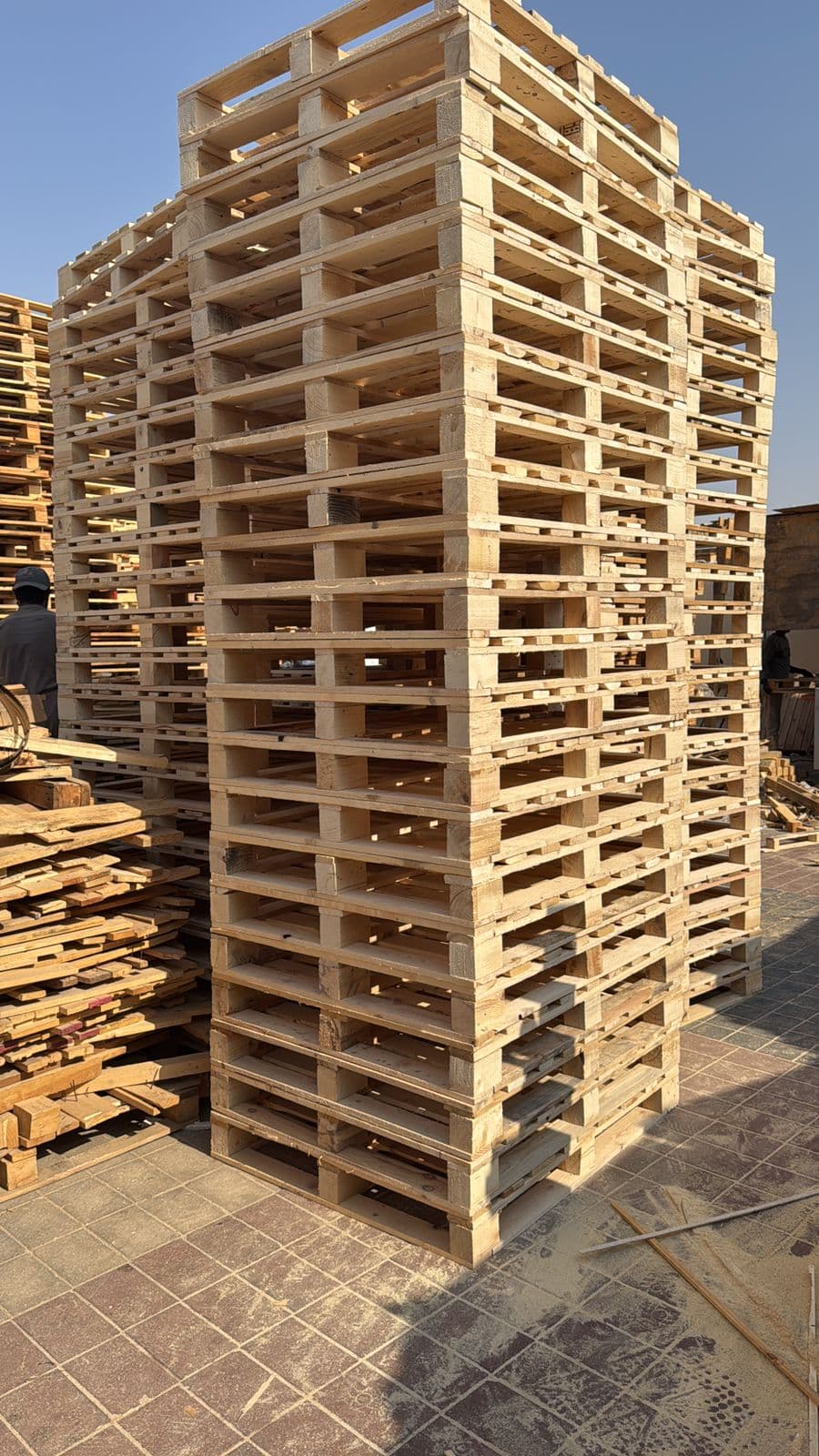 A large square stack of used pallets beside offcut boards kept for repairs