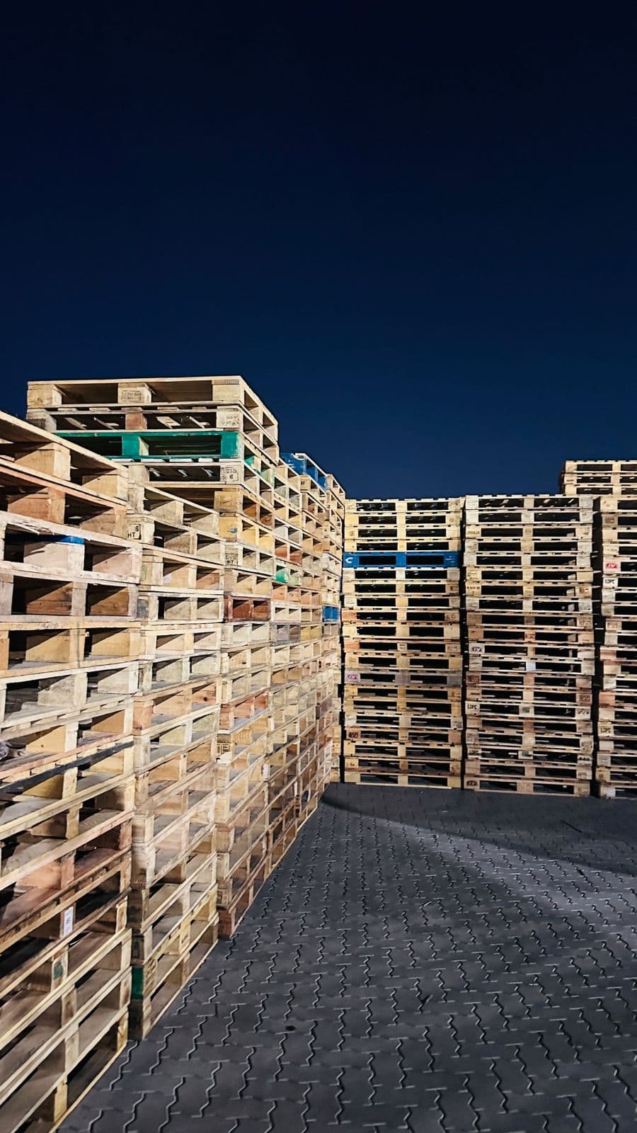 Used wooden pallets stacked in the yard at night, many carrying HT stamps
